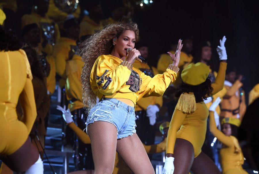 Beyoncé Knowles Carter performing at Coachella in her iconic yellow crop top and jean shorts outfit in 2018. 