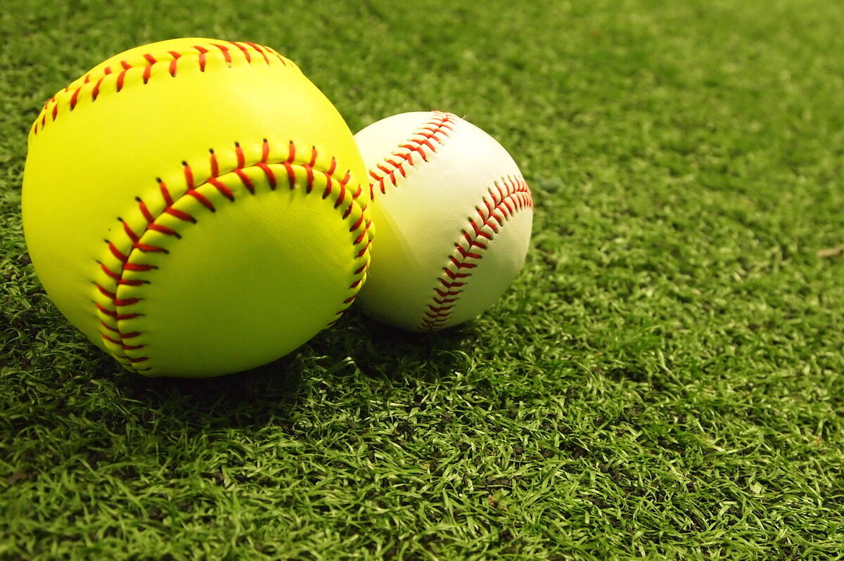 A baseball and softball lie adjacent to each other.